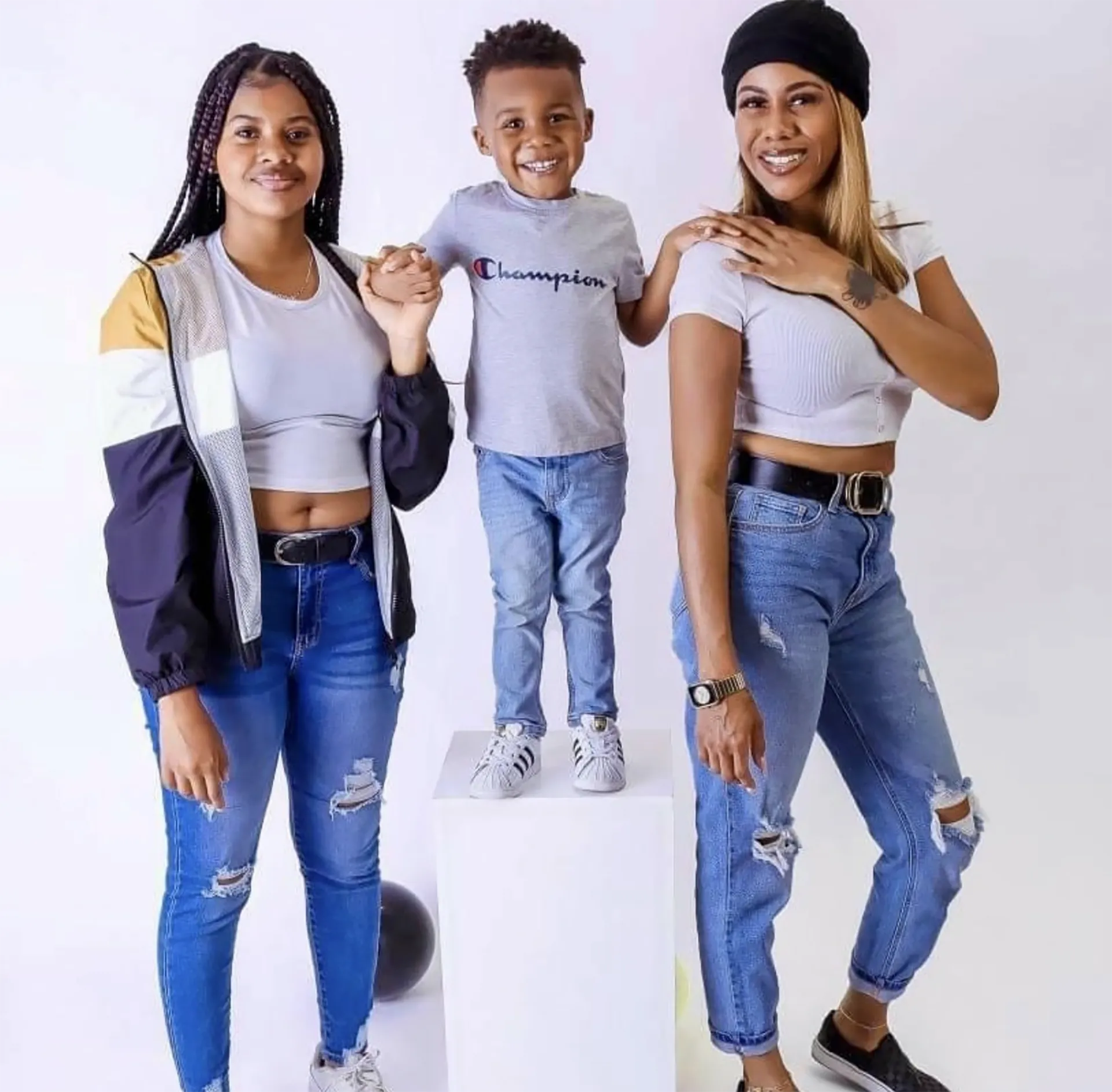 two Black woman with a kid standing over a box in the middle of them